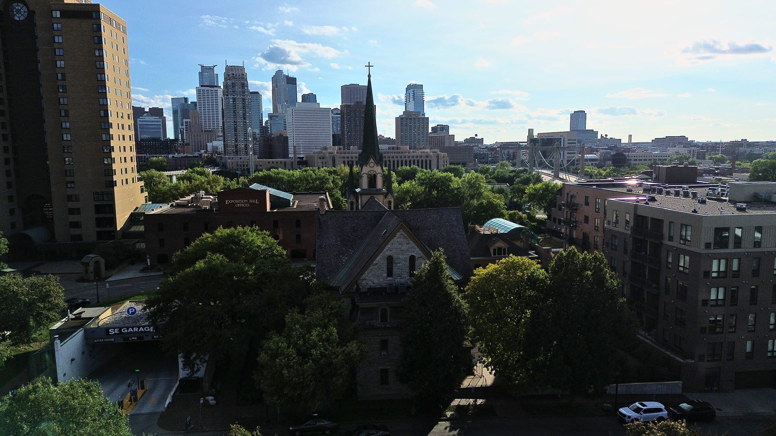 Northeast Minneapolis from above: a church steeple and rooftops, with downtown behind them. Photographed by Spencer Bernauer.